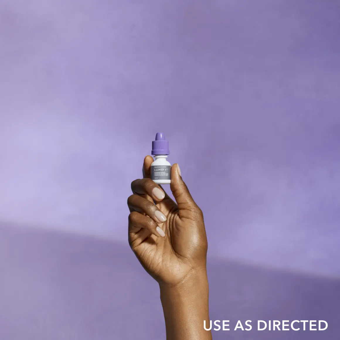 A hand holding up a Lumify eye drop bottle